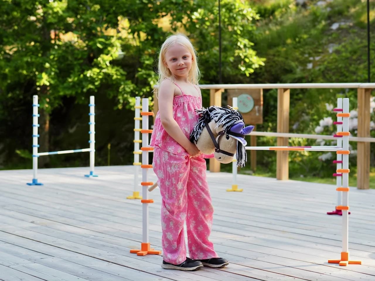 Lapsi poseeraa keppihevosen kanssa Hoppi-hyppyesteradan keskellä thumbnail
